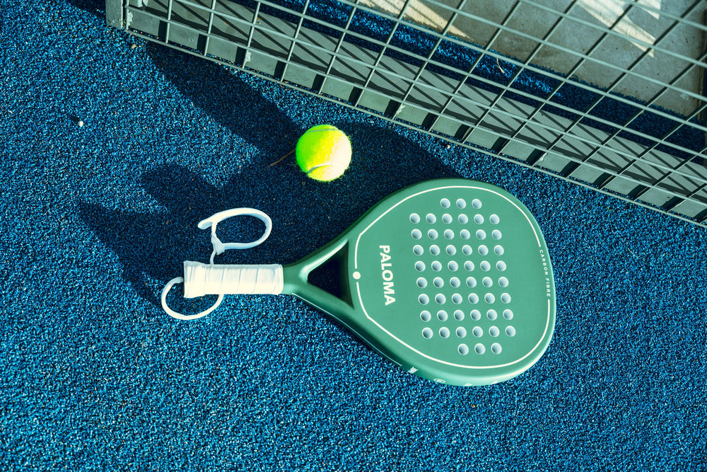 Ivory Green Paloma racket and wrist strap on court; ball shown as a prop