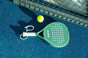 Ivory Green Paloma racket and wrist strap on court; ball shown as a prop