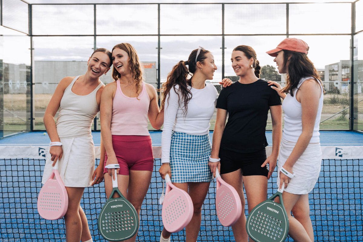 Friends laughing together on a padel court with Paloma Pink and Ivory Green rackets